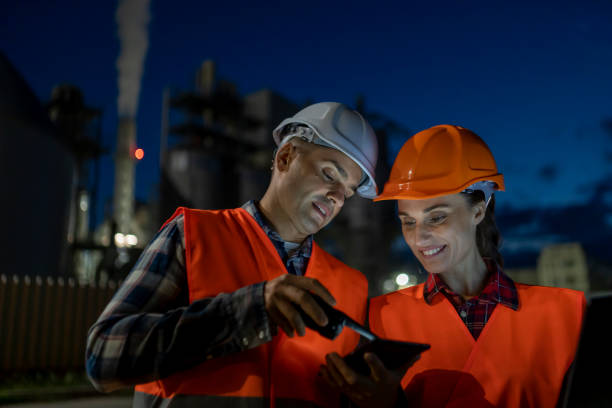 Two night shift engineers use a tablet and a laptop in the refinery.